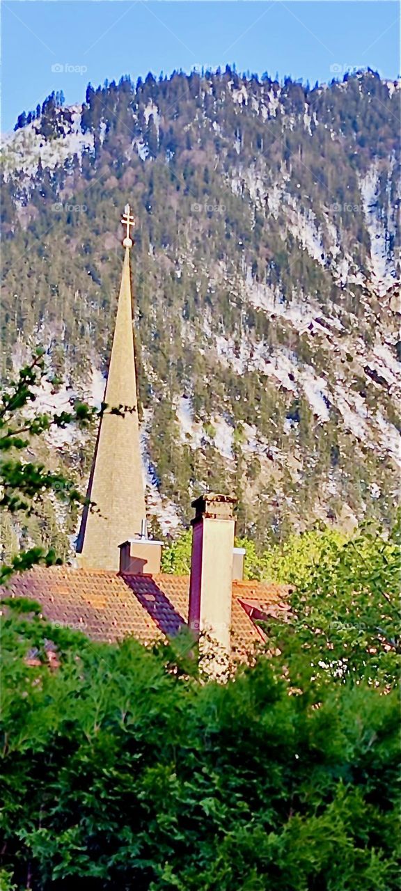 This church steeple and adjacent buildings is part of „Bayerischzell“, a small township near the Alps in „Bavaria“, Germany. The picturesque mountainous setting is quite intriguing and inviting to travelers of all kinds. 2024. Hypnotic Productions