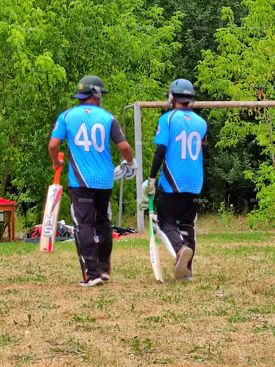 cricket training.  two players in gear are walking from the field to rest