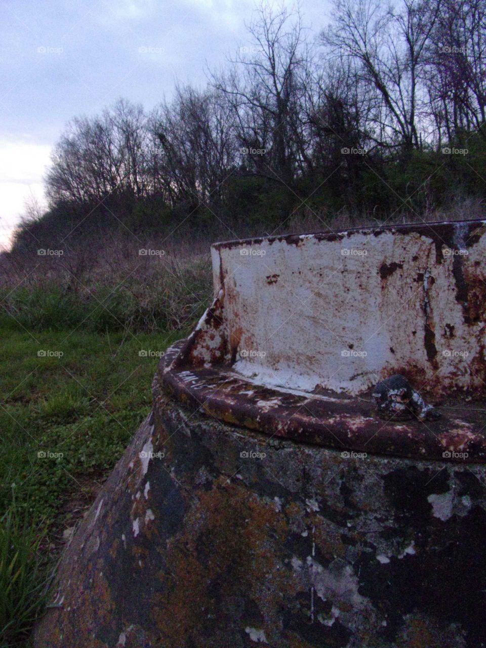 Sewage access in the middle of a field surrounded by trees.