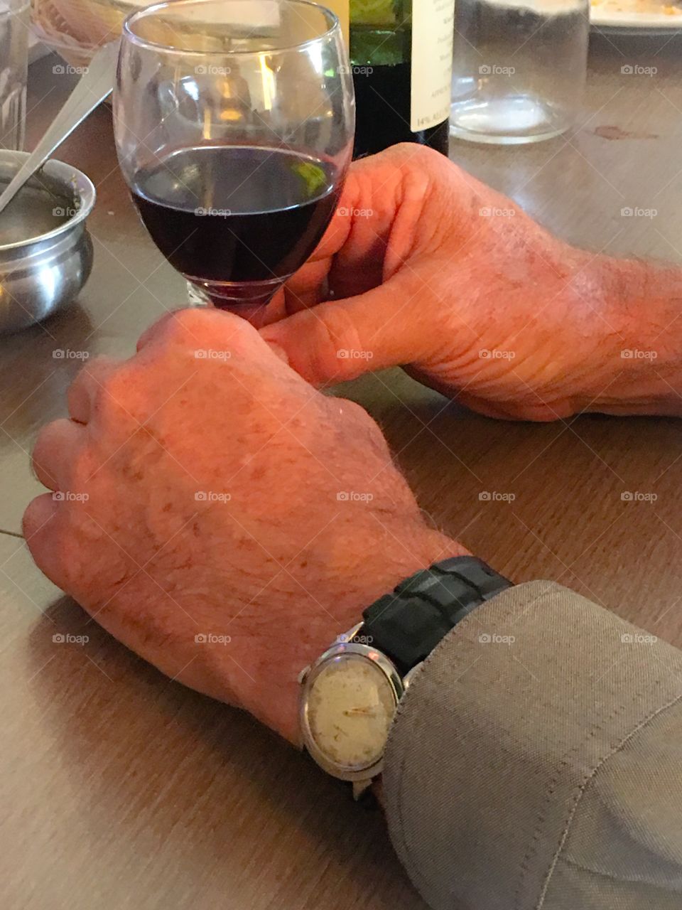 Close up view of mature elderly person's hands on table, holding stem of glass of wine, wind up vintage watch on wrist