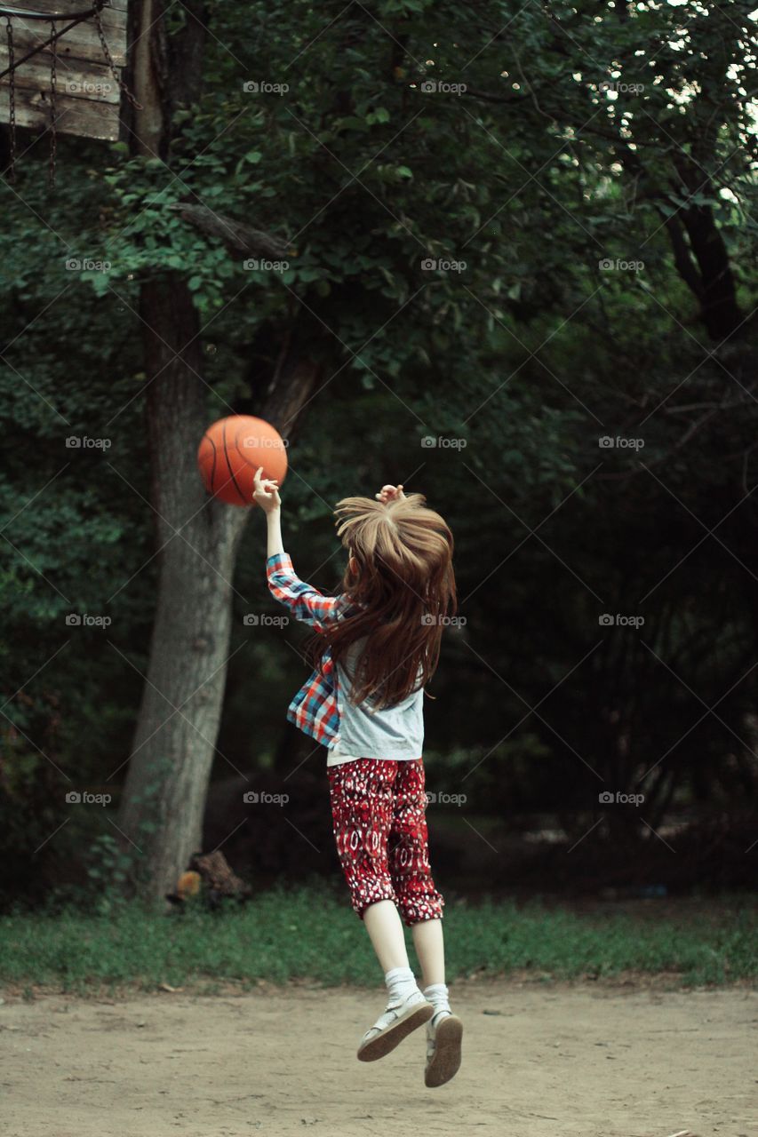Girl playing basketball throws a ball into the ring in a jump