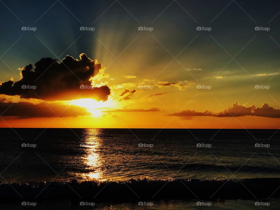 Spectacular golden sunset through dark clouds reflecting on the Ocean.