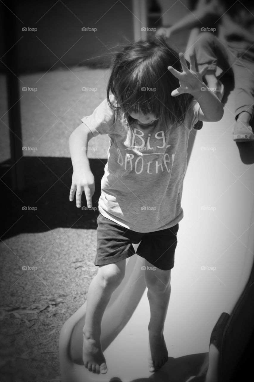 A joyful, young child leaps with energy from a slide on a playground