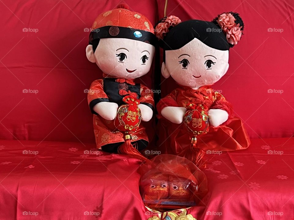 Chinese plush dolls marriage couple in the room of newly weds on a red bed with red shoes for the baby to come.