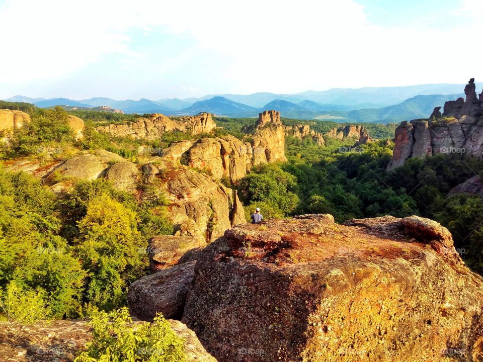 A beautiful scenery in Bulgaria with its beautiful nature in the Belogradchik rocks with the mountain hills in the back and amazing structures in the forests and a man sitting in the centre of it all