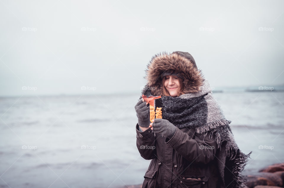 Happy girl in warm winter clothing enjoying peanuts at the beach.