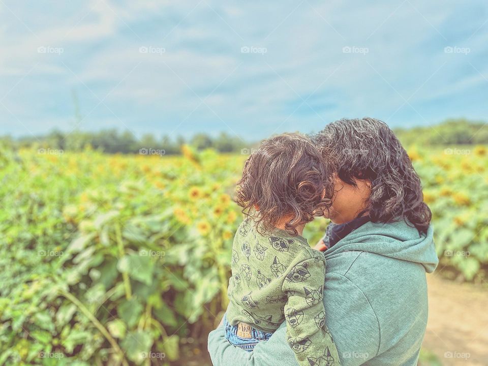 Mother and daughter stand in field of sunflowers, mother shows baby sunflowers, going to a sunflower field for the first time, excited about flowers, sharing nature with our children