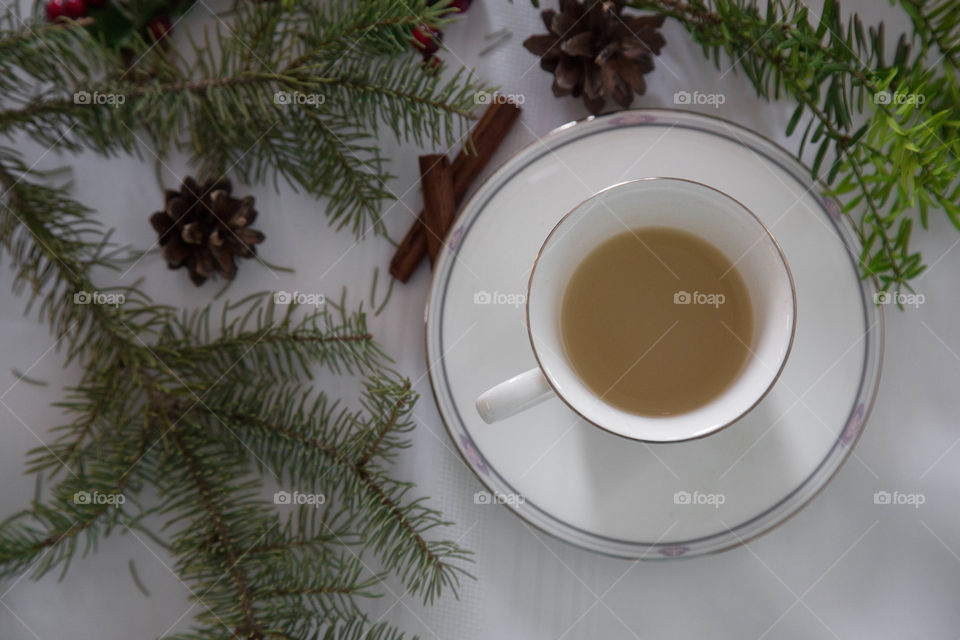 Tea cup and saucer flat lay on white table surrounded by earthy, festive pine