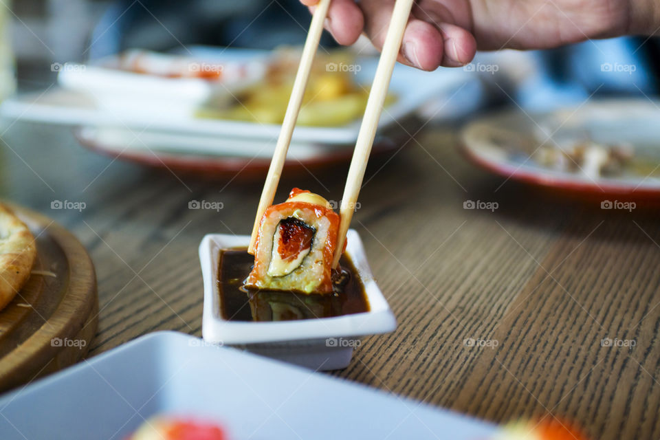 Eating roll sushi in japanese restaurant, hand with chopsticks