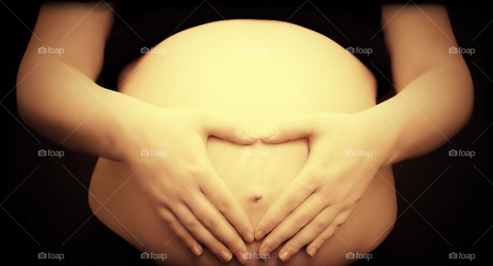 Woman making heart shape with her hands on her pregnant belly