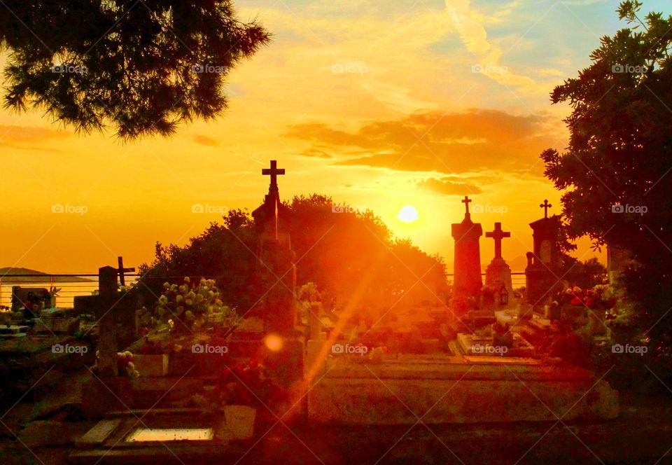 Vivid orange sunset with ray of sunshine and silhouettes of crosses on gravestones with sea in the background