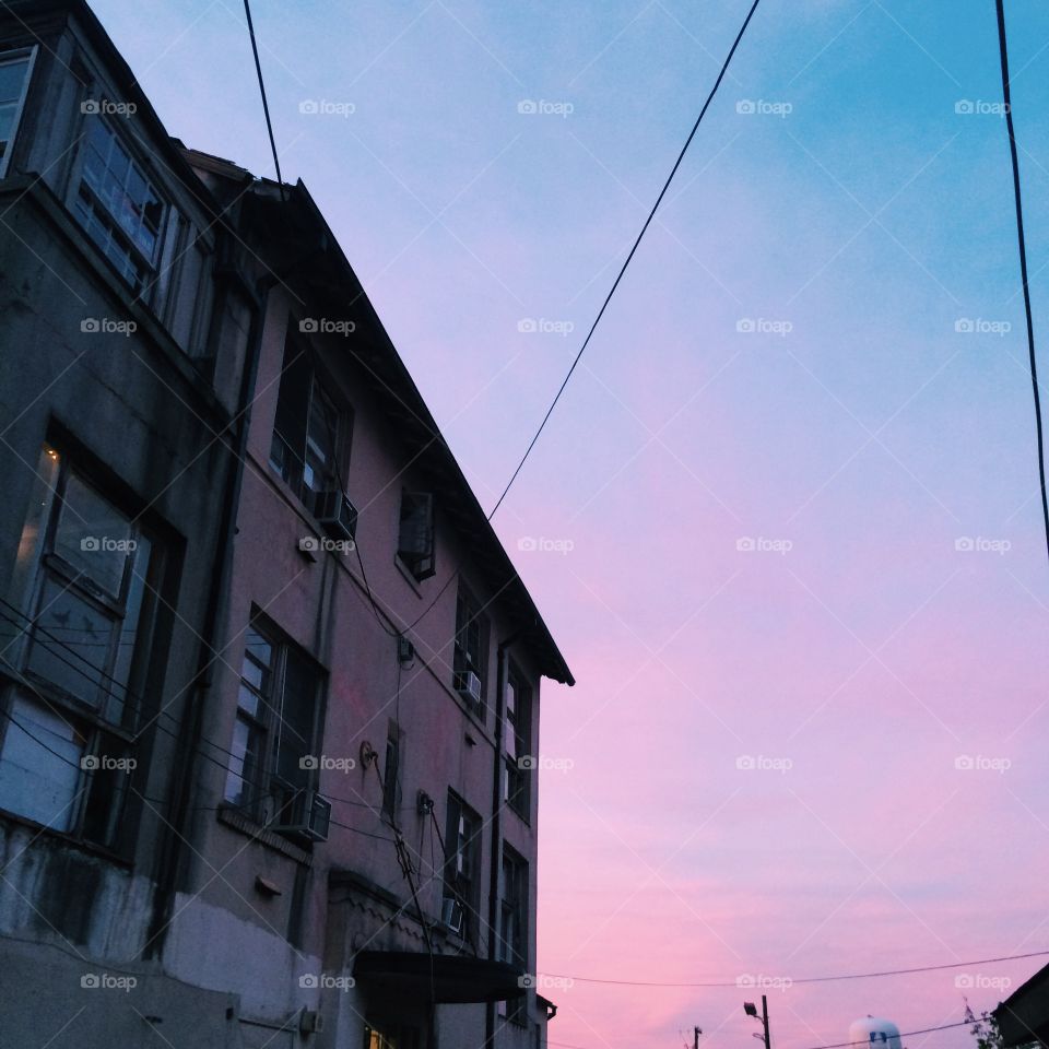 Urban sunsets, soft pastels, lavender and rose hues across the city sky. Golden light streaking through the windows of a studio apartment