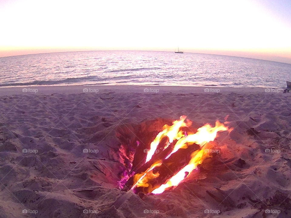beach Bonfire with purple flame.... With ocean and sailboat in background