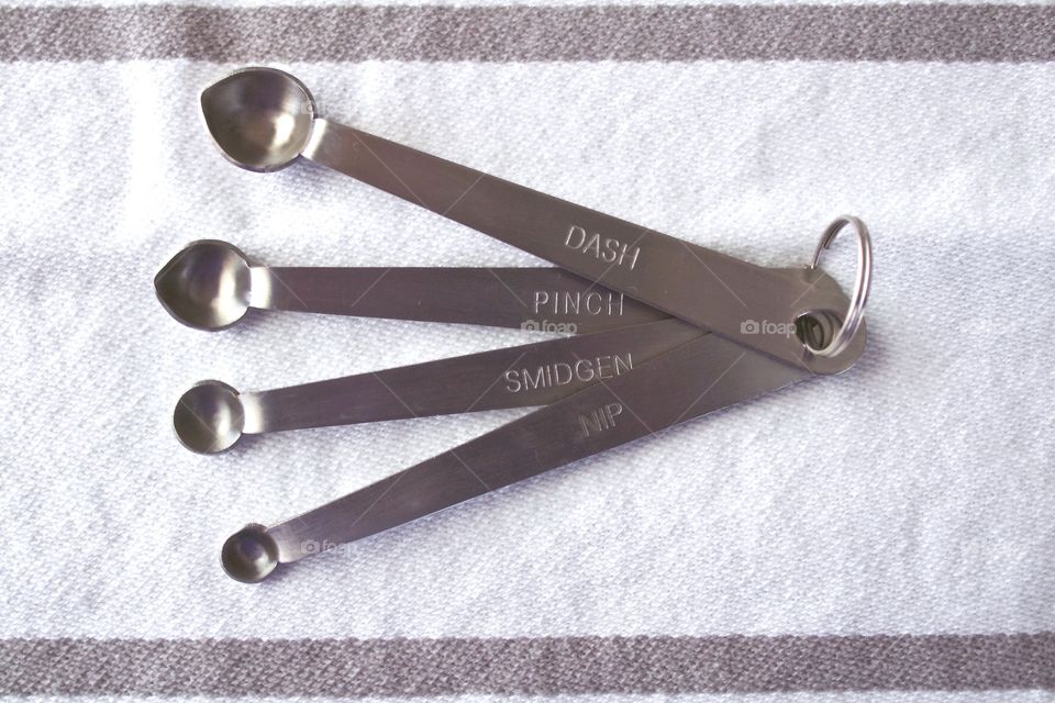 Overhead view of miniature stainless steel measuring spoons on a white-and-grey-striped dish towel