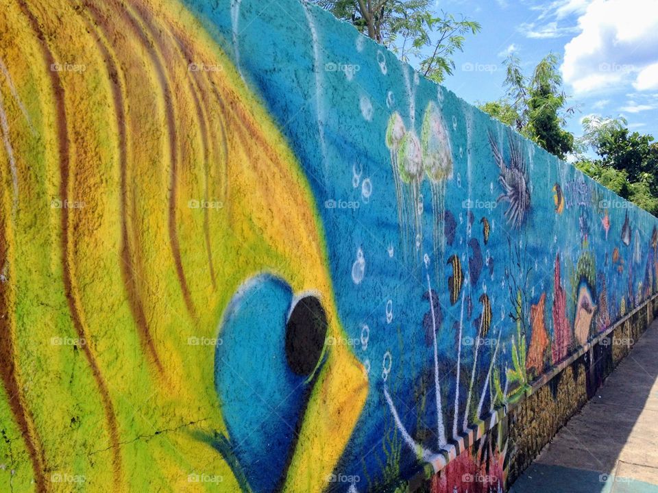 Perspective view to the blue and yellow bright contrast underwater theme graffiti mural on the cement fence wall