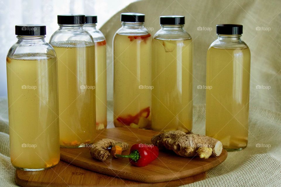 Homemade kombucha, bottled for a second ferment, flavored with slices of turmeric root, red chili pepper, and / or ginger root on stacked bamboo cutting boards