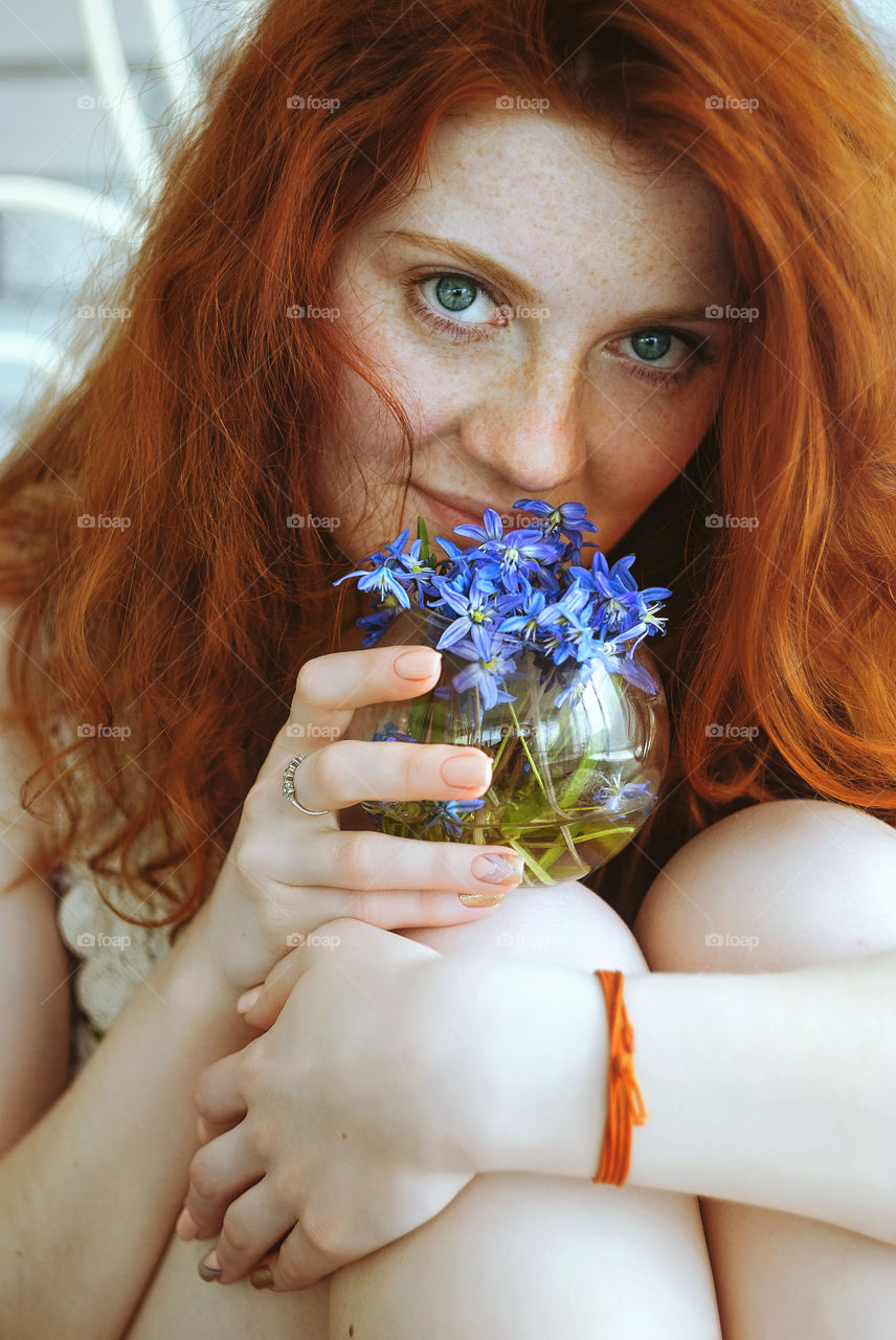 Redhead young woman with freckles and blue eyes sitting and looking to camera.