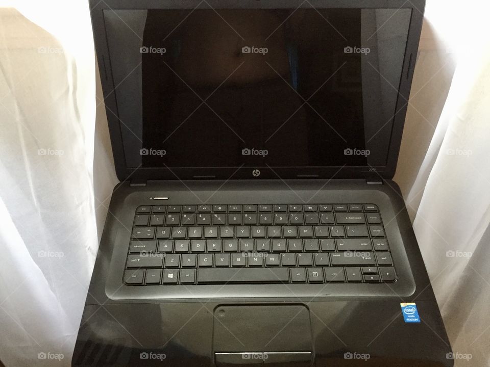 A laptop computer in front of a window with white sheer curtains