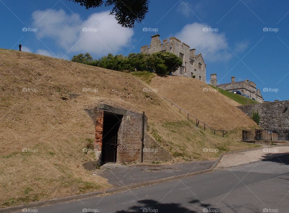 Part of the Dover Castle on a hill in England with an entryway at the bottom of the hill on a summer day. 