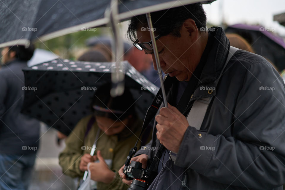 Asian man standing with umbrella looking at camera