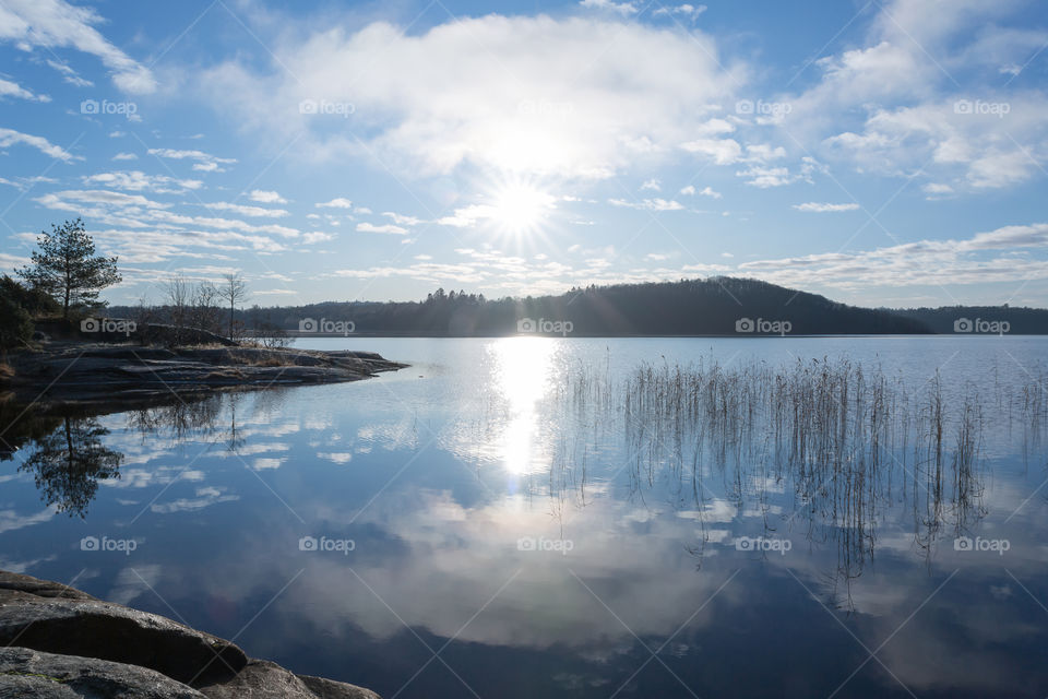 Beautiful sunny day with sun and cloud reflection in mirror lake, Swedish landscape 