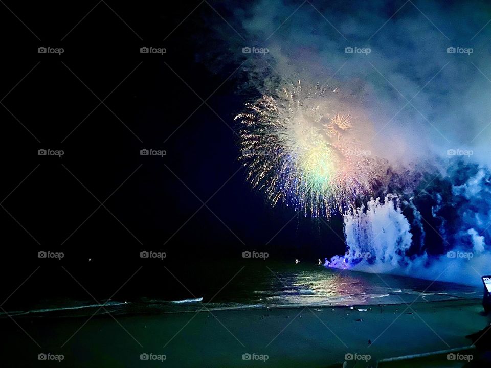 Fireworks bursting over the ocean very enhanced against the backdrop of cool summer night 