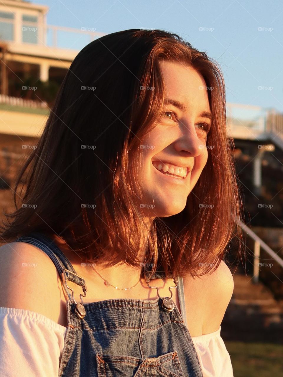 A warm summer sunset illuminates the face of a young woman with a joyous smile