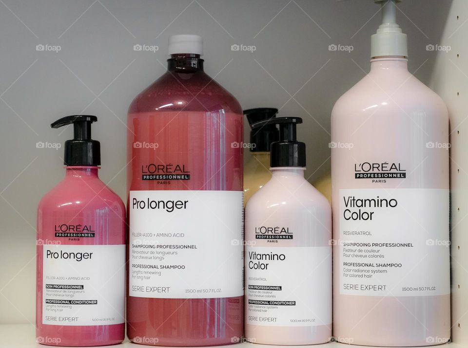 Four large bottles with dispensers of hair cosmetics brand L'Oreal stand in a row on a shelf of a wall-mounted white cabinet, close-up side view. Concept of a hairdressing salon, hair cosmetics, beauty salon