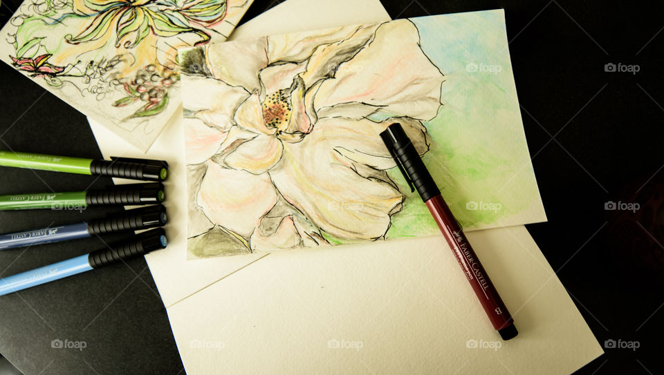 Faber-Castell PITT artist pens on desk with watercolor style painting sketch using Faber-Castell pens high angle view of spring flowers on sketch books 