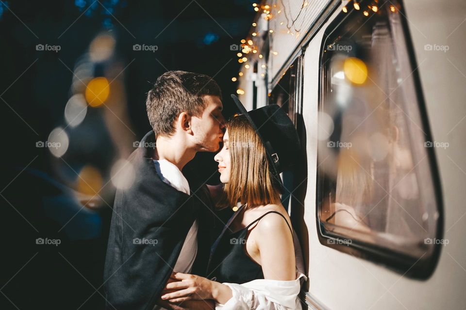 Young couple in love in stylish fashionable outfit romantic weekend wedding trip against background of camper in woods forest road trip