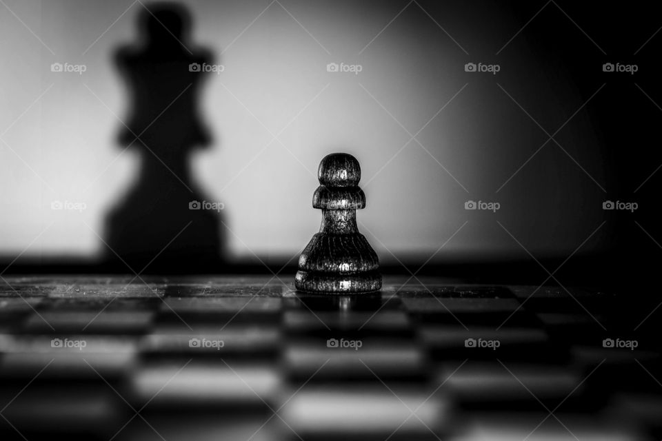 Black pawn with a shadow of a queen on a chess board