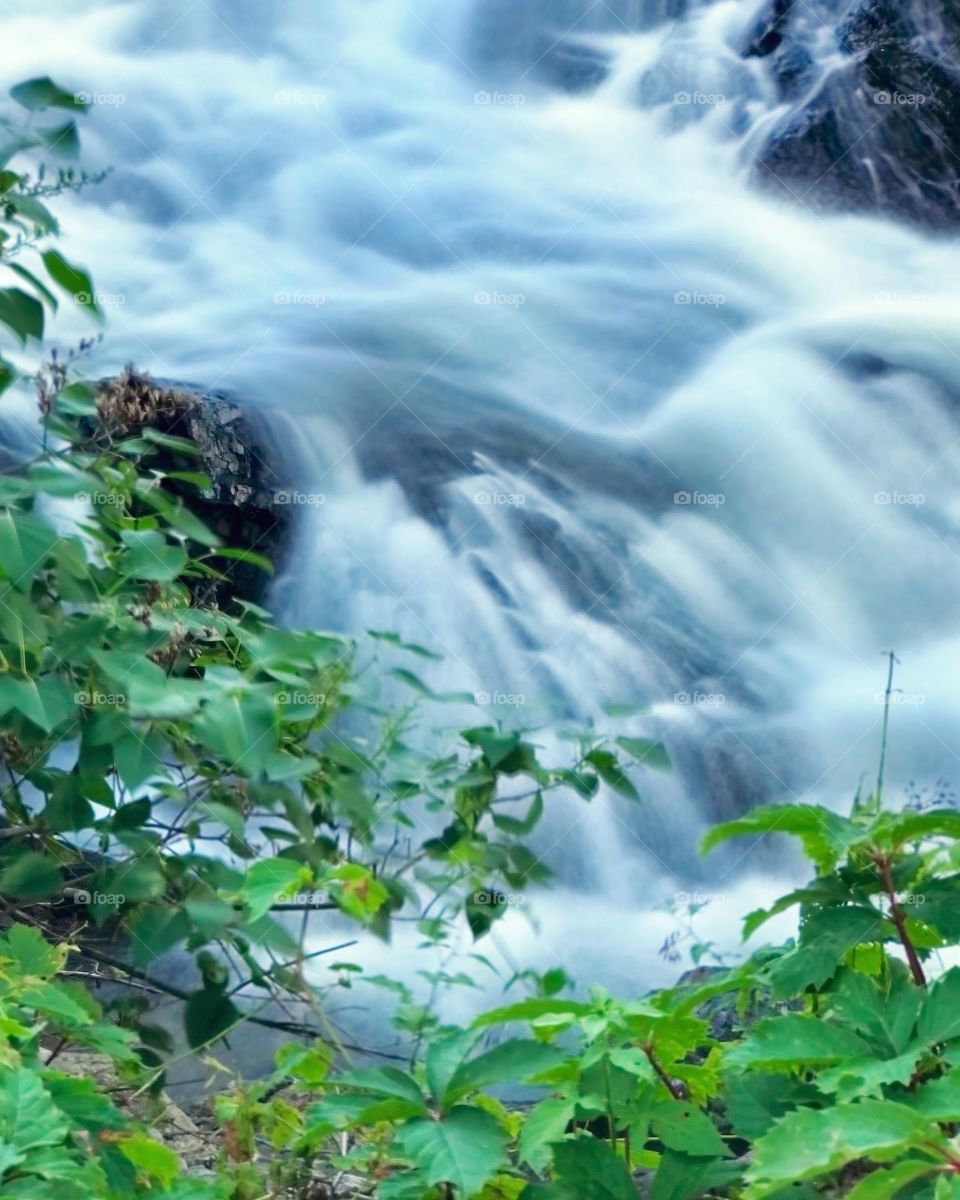 Waterfall with rushing water flowing over rocks into the river at Camden Harbor in Camden, Maine. Shot on iphone and edited as a long exposure. 