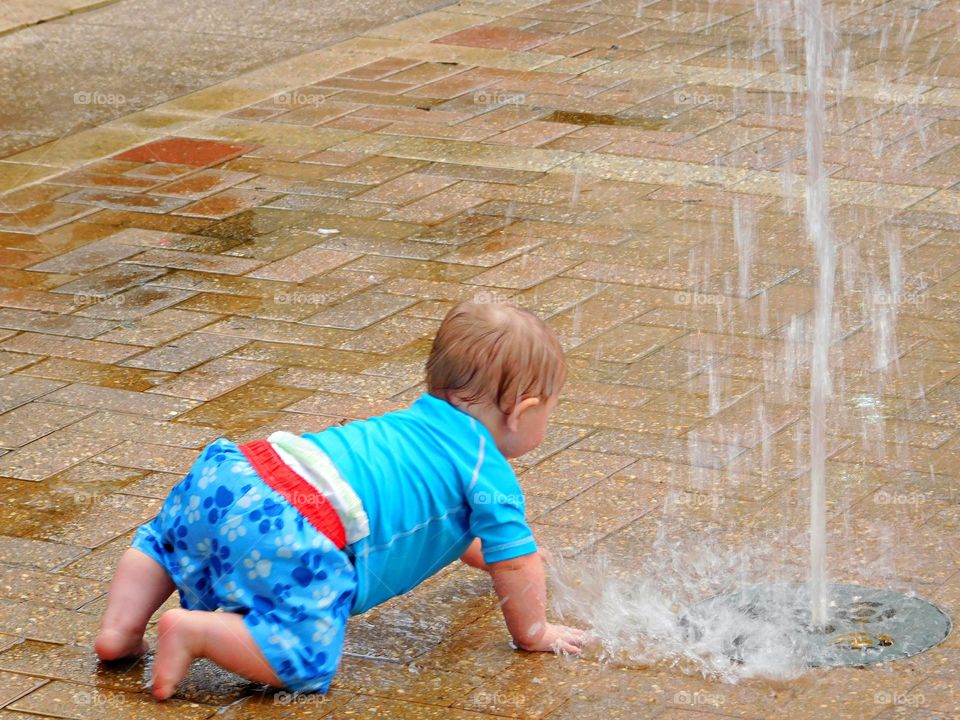 Urban Nature: Water - A baby enjoys the stream of water - A fountain is an ornamental feature in a pool or lake which consists of a long narrow stream of water that is forced up into the air by a pump.