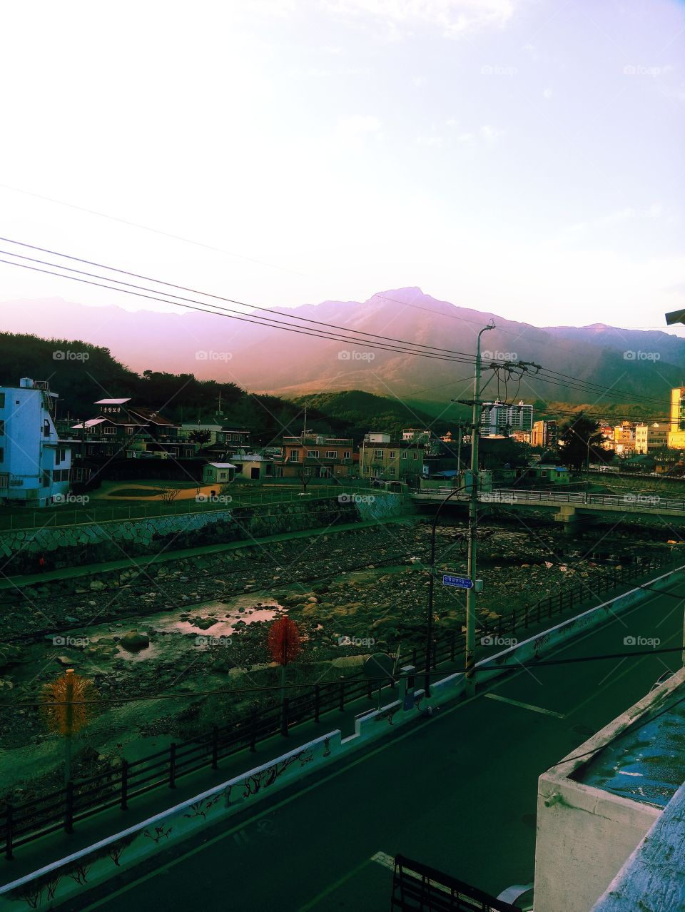 The scenery at my home town with the river, bridge, houses ,buildings and a very high mountain that u can see far that is half covered by Sunlight.
this is the sunset time.
