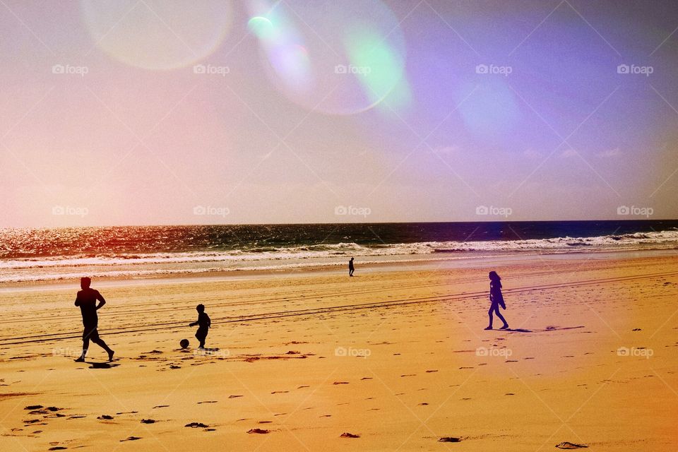 A family play on a beach just as the sun is setting. 
