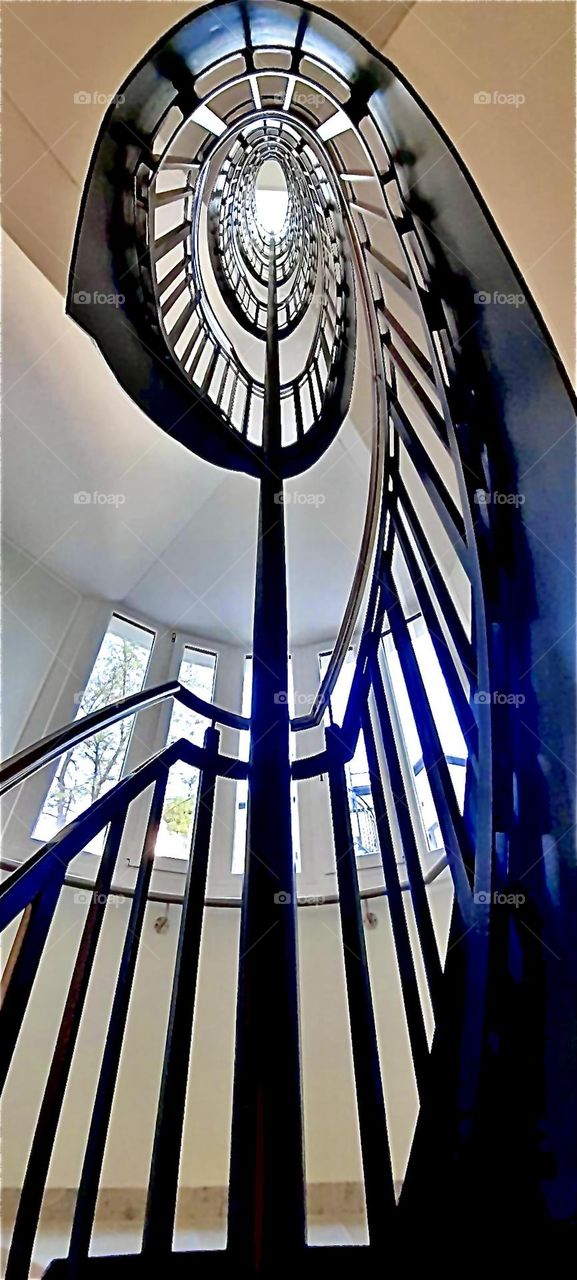 A spectacular spiral staircase winds its way up to the higher floors of an old building in „Munich“, „Bavaria“, Germany. The nostalgic influence shows in the rounded tower like part with multiple narrow windows. 2022. Hypnotic Productions