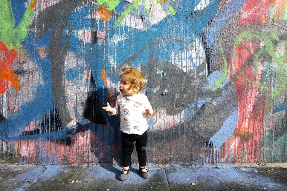 Baby girl standing in front of graffiti wall