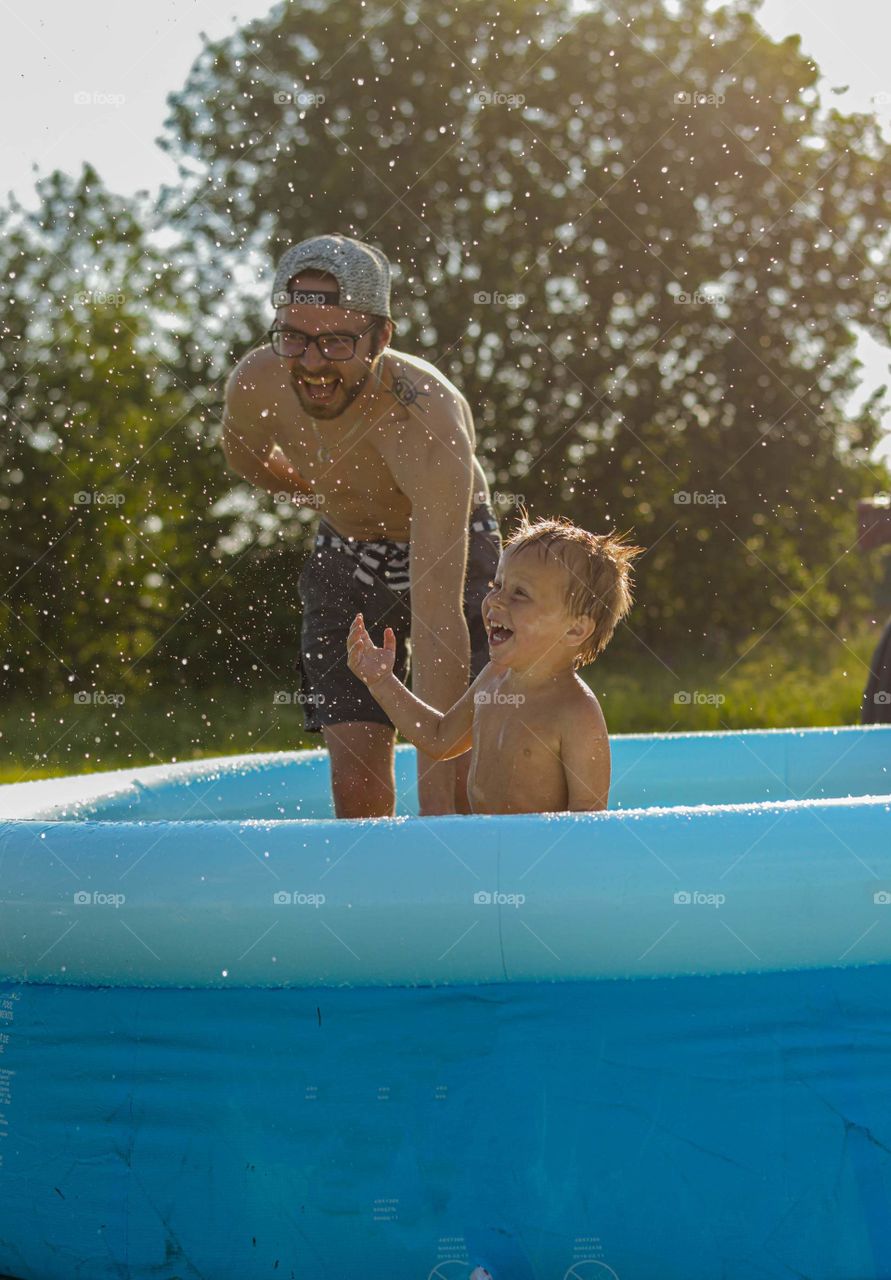 Toddler nd his uncle playing in the pool at hot sunny summer day.