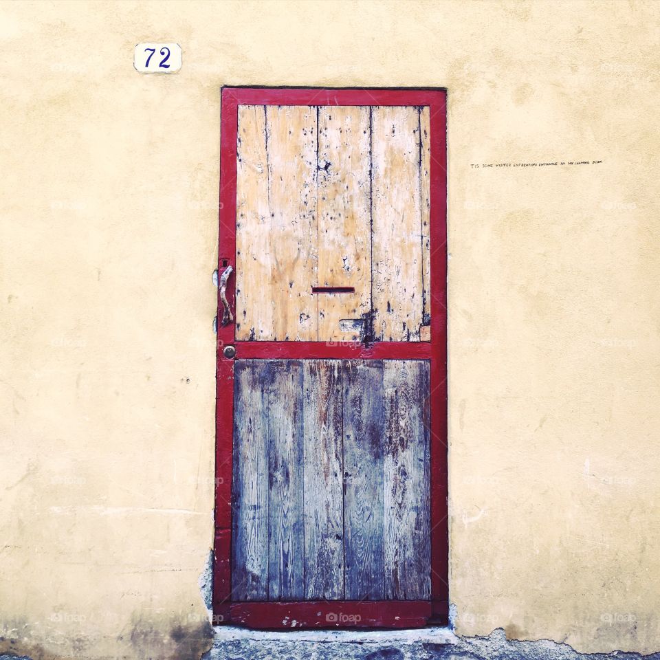 A red wood framed door on an ecru wall in Lucca, Italy