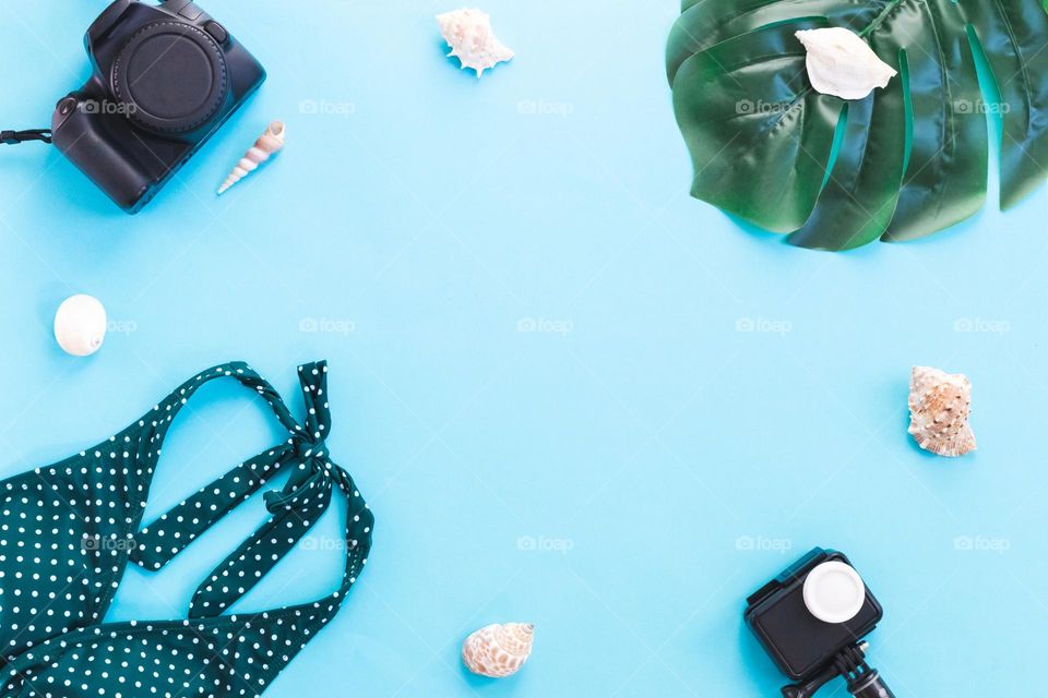 A swimsuit with polka dots, two cameras, shells and a monstera leaf lie in a round frame on a stncm background with copy space in the center, a flat lay close-up.