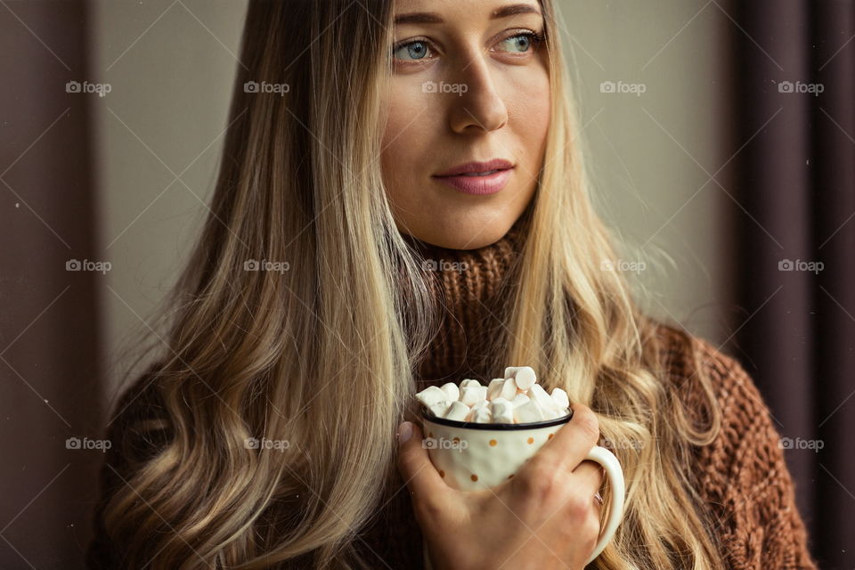 Portrait of young woman with long blonde hair. She holding cup of coffee with marshmallow 