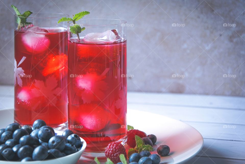 A glass of juice with ice and a blueberry and strawberry in plate