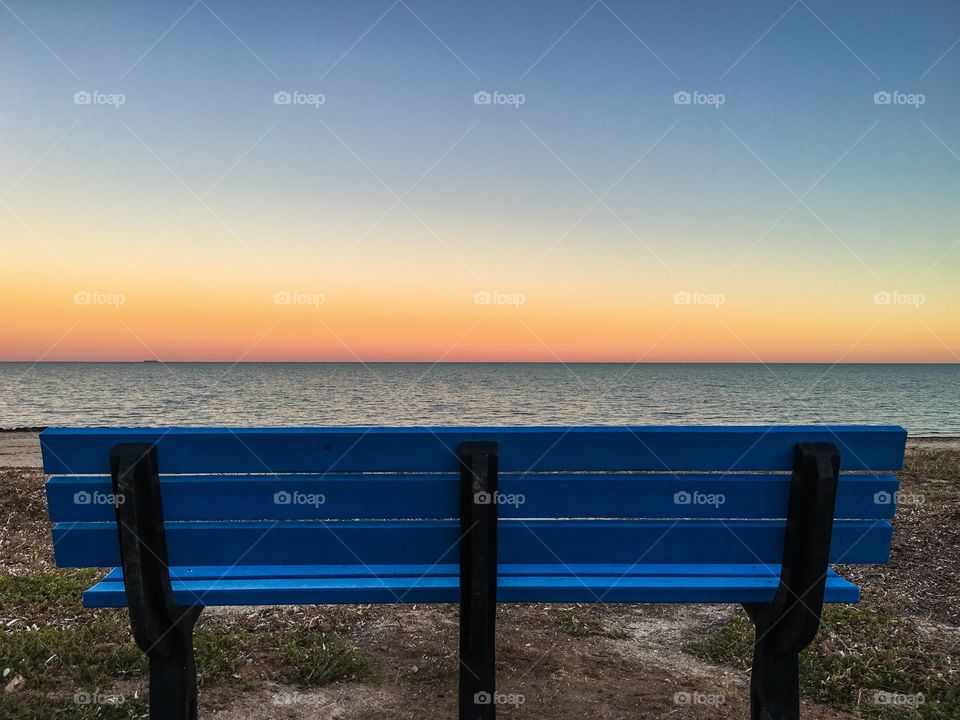 Blue bench on beach at sunset