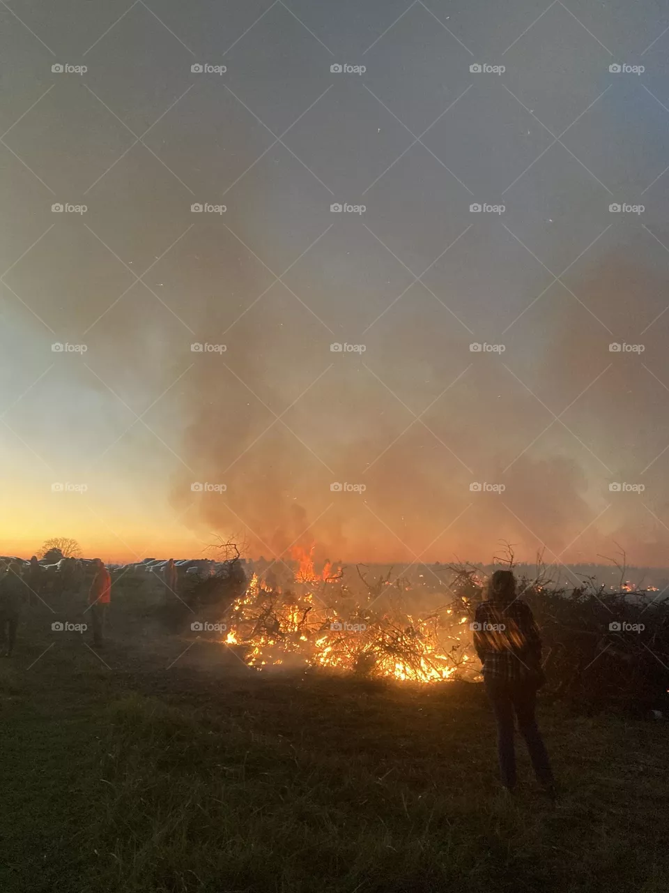 Smoke and flames rise in a twilight sky from burning brush as the evening chill sets in.. 