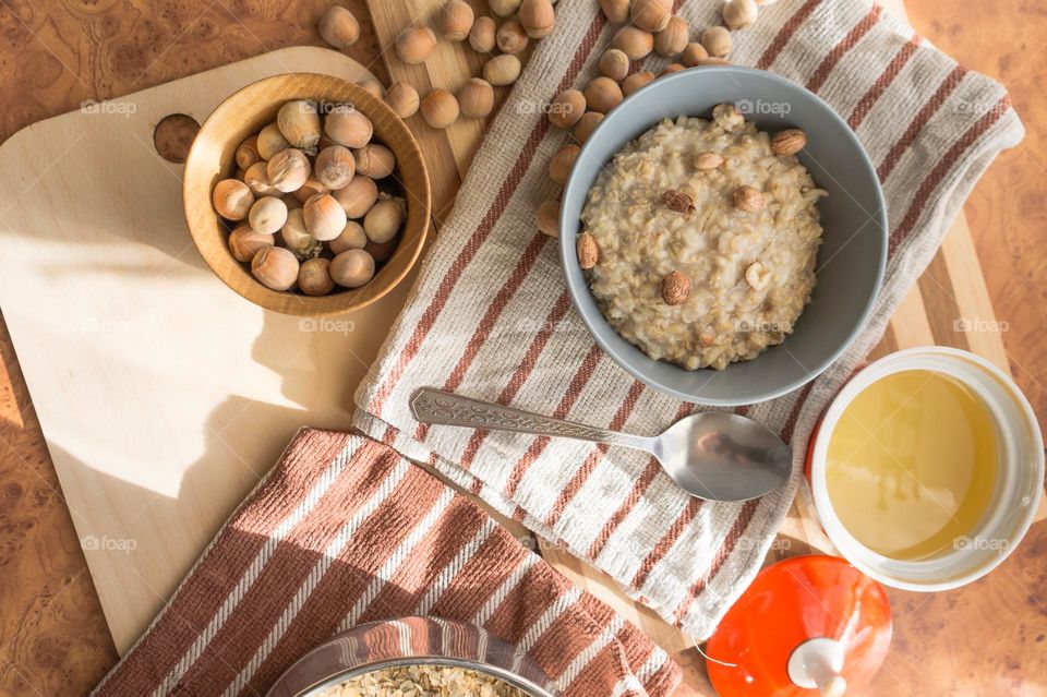 Cooked oatmeal in a deep gray plate with hazelnuts and honey.