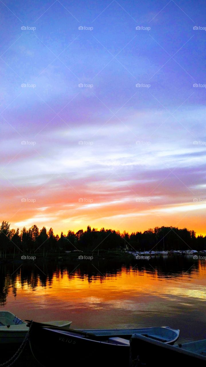 Colorful sunset evening sky. Water illustrates The sky. Small boats by the water. Blue purple orange yellow sky.