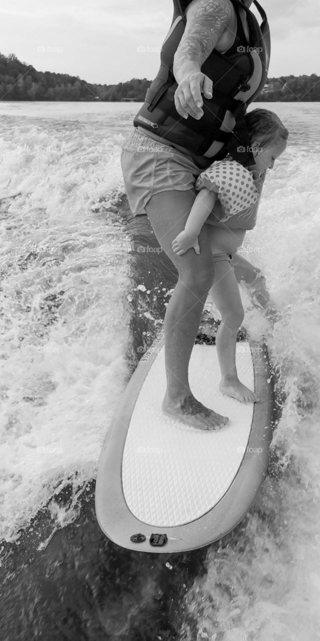 Woman teaches a little girl to wake surf behind a boat in the lake.
