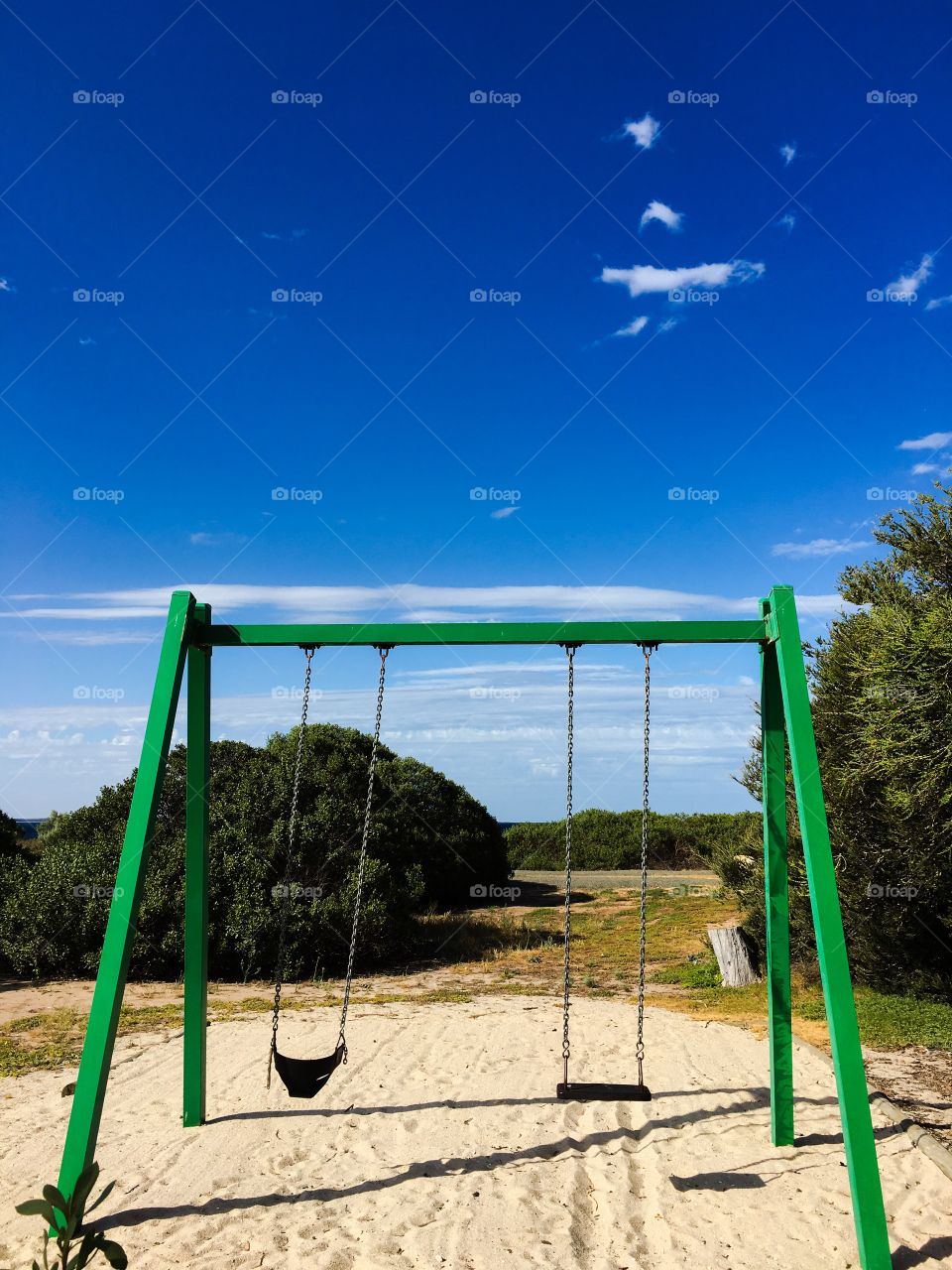 Outdoor swing set in park, ocean on horizon, blue sky