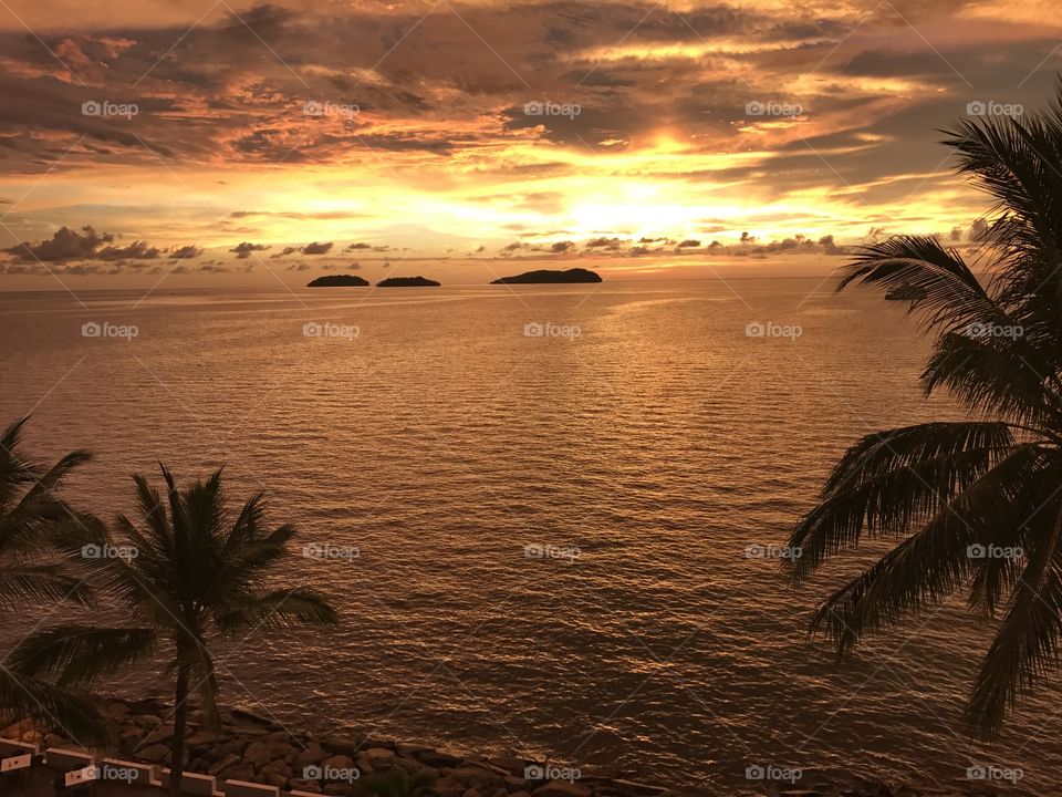Beautiful Golden orange sunset sky overlook small islands in Sabah, Malaysia with palm trees