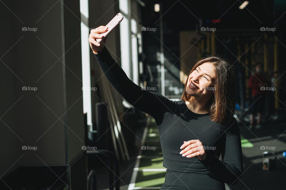 Portrait of resting Young brunette woman in sport active wear taking selfie in fitness club gym